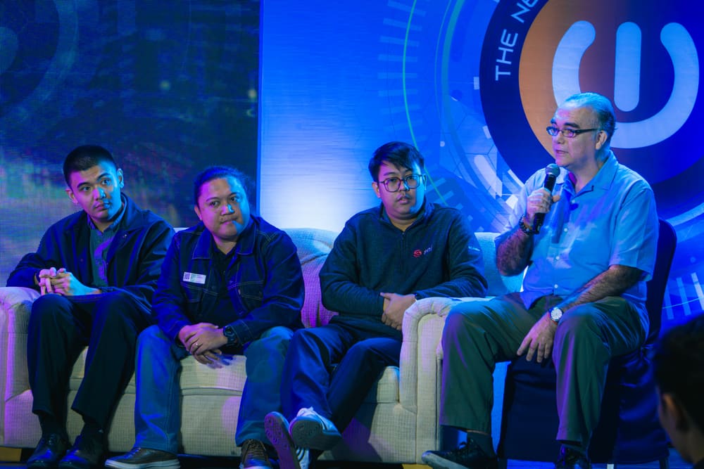A panel of four people seated together on stage, with one panelist speaking into a microphone.