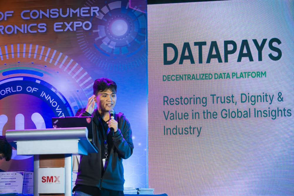 A speaker at a podium gesturing while presenting a slide about a decentralized data platform at an expo.